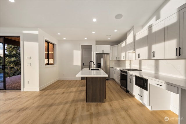 kitchen featuring a center island with sink, white cabinets, decorative backsplash, appliances with stainless steel finishes, and light hardwood / wood-style floors