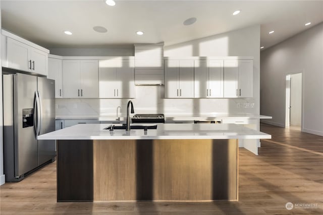 kitchen featuring white cabinetry, sink, stainless steel fridge with ice dispenser, backsplash, and an island with sink