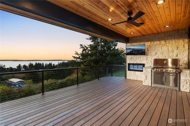 deck at dusk featuring a water view, area for grilling, ceiling fan, and a grill