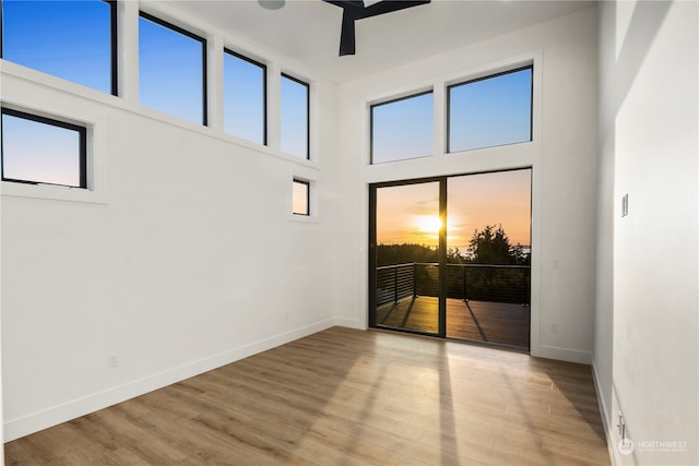 empty room with ceiling fan, light hardwood / wood-style floors, and a towering ceiling