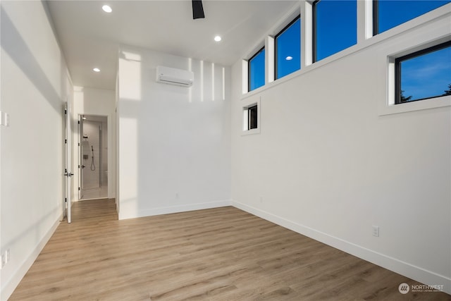 interior space with a high ceiling, light hardwood / wood-style floors, and a wall mounted air conditioner