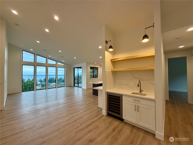 kitchen with white cabinetry, sink, hanging light fixtures, beverage cooler, and light wood-type flooring