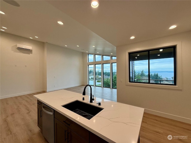 kitchen featuring light stone countertops, dishwasher, sink, an island with sink, and light wood-type flooring