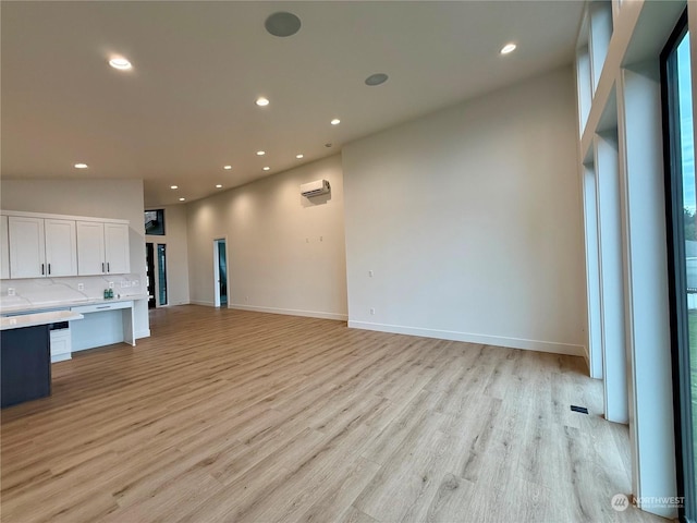 unfurnished living room featuring a towering ceiling, a wall mounted AC, and light hardwood / wood-style flooring