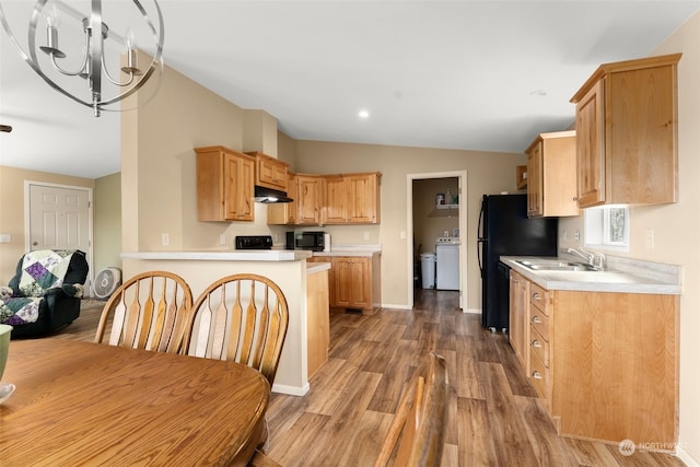 kitchen featuring kitchen peninsula, vaulted ceiling, a chandelier, washer / dryer, and hardwood / wood-style floors