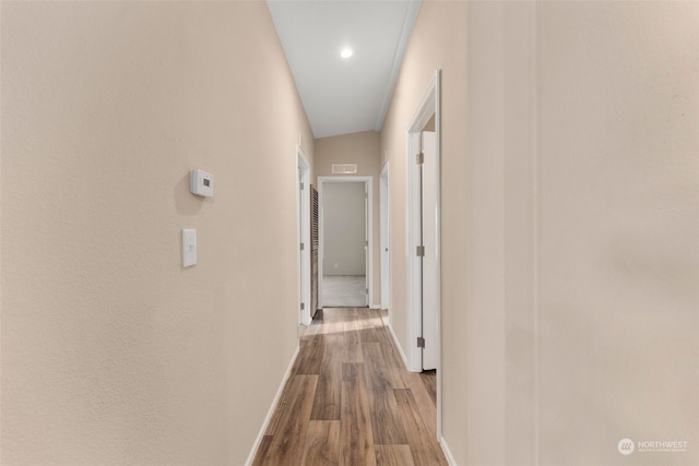 corridor with light wood-type flooring and vaulted ceiling