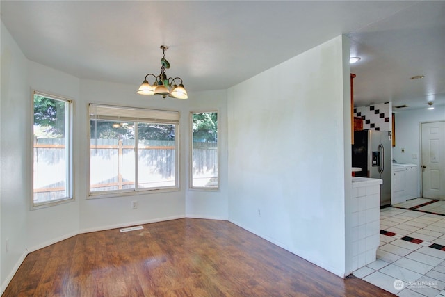 unfurnished dining area with a notable chandelier, light wood-type flooring, and washing machine and clothes dryer