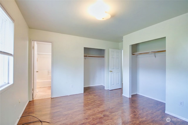 unfurnished bedroom featuring multiple closets, ensuite bath, and dark hardwood / wood-style flooring