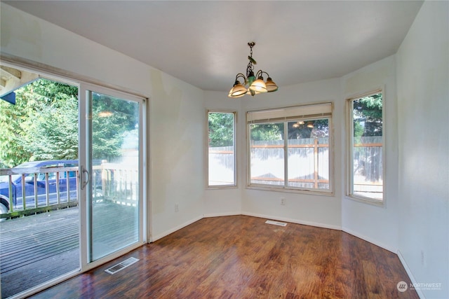 unfurnished dining area with a notable chandelier, dark wood-type flooring, and a healthy amount of sunlight