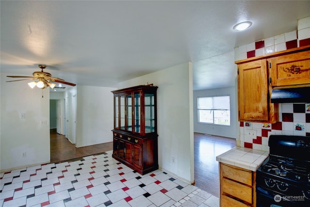 kitchen with decorative backsplash, light hardwood / wood-style floors, ceiling fan, gas stove, and tile counters