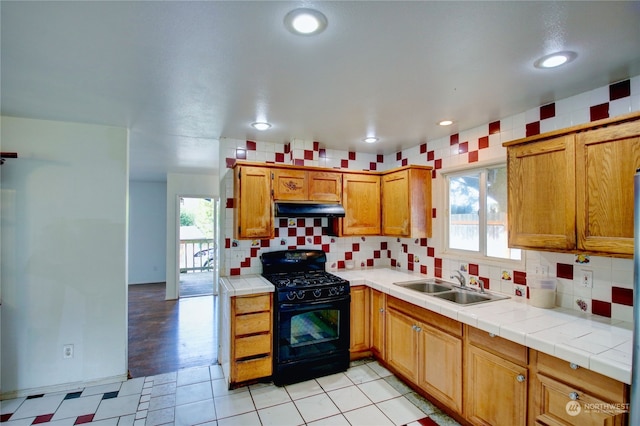 kitchen featuring a wealth of natural light, tile countertops, black gas range oven, and sink