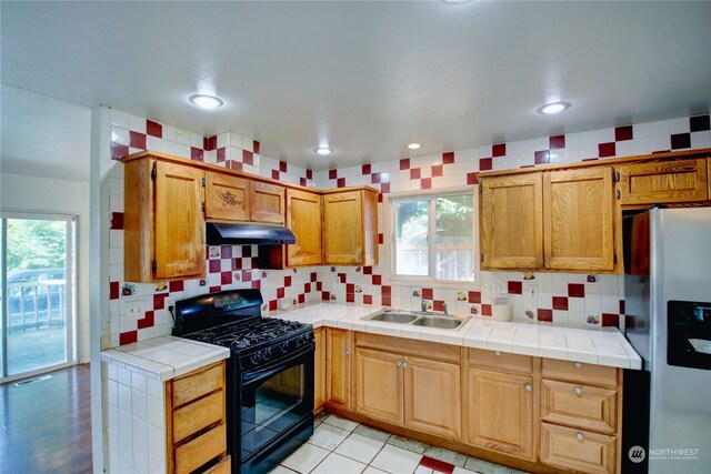 kitchen featuring tile counters, sink, stainless steel refrigerator with ice dispenser, decorative backsplash, and black range with gas cooktop