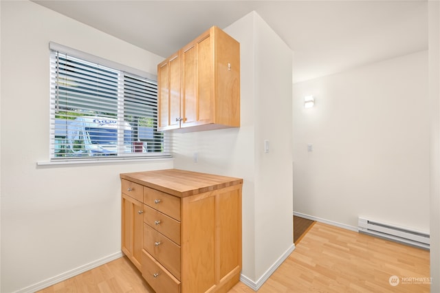 kitchen featuring light wood-type flooring, butcher block counters, baseboard heating, and light brown cabinetry