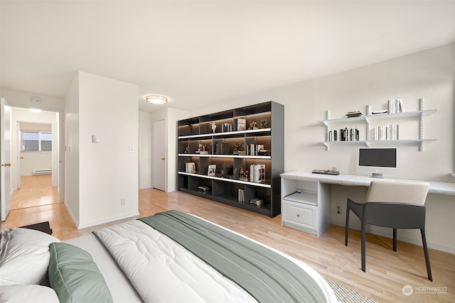 bedroom with built in desk, a baseboard radiator, and light hardwood / wood-style flooring