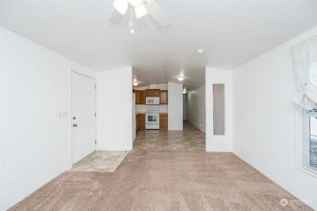 unfurnished living room featuring vaulted ceiling, ceiling fan, and light carpet