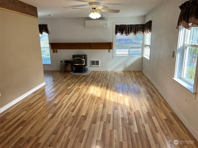 unfurnished living room with ceiling fan, a wood stove, wood finished floors, and a wall unit AC