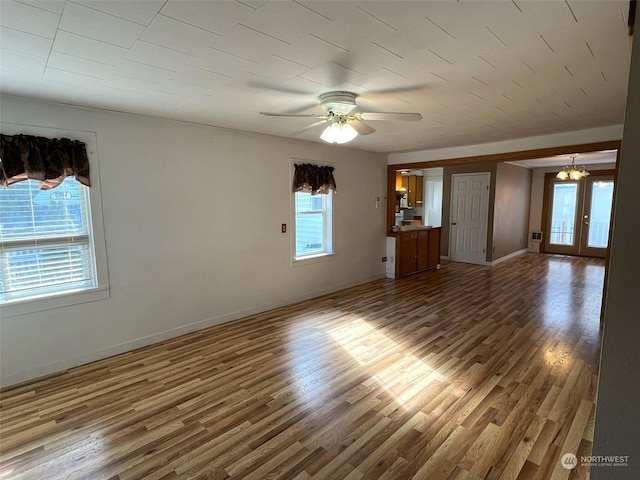 unfurnished living room featuring ceiling fan with notable chandelier, plenty of natural light, baseboards, and wood finished floors
