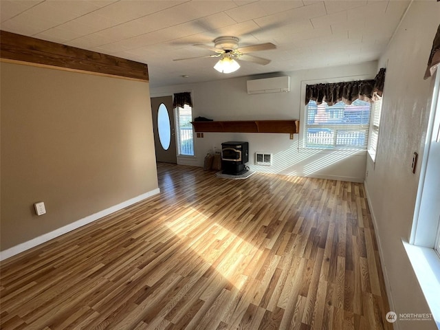 unfurnished living room with visible vents, a wealth of natural light, a wood stove, and a wall mounted air conditioner