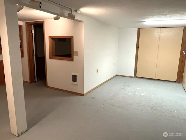finished basement featuring rail lighting, baseboards, and heating unit