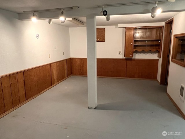 finished below grade area featuring track lighting, wainscoting, and wooden walls