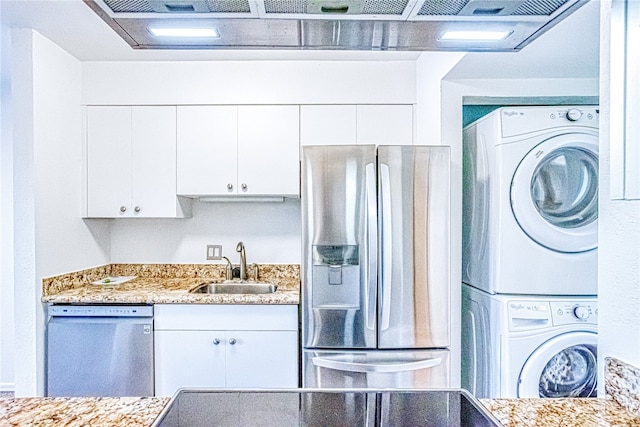 kitchen featuring sink, white cabinetry, stacked washing maching and dryer, appliances with stainless steel finishes, and light stone countertops