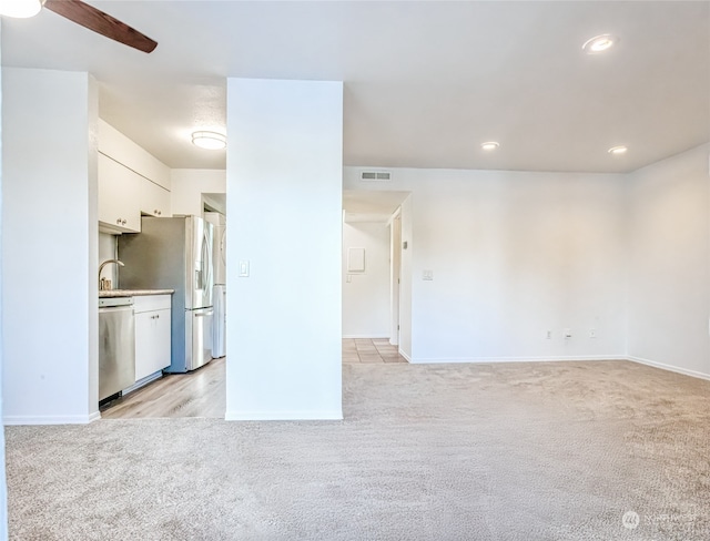 interior space with appliances with stainless steel finishes, ceiling fan, light carpet, and white cabinets