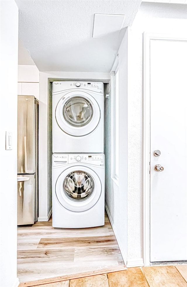 laundry area with stacked washer and clothes dryer, a textured ceiling, and light hardwood / wood-style flooring