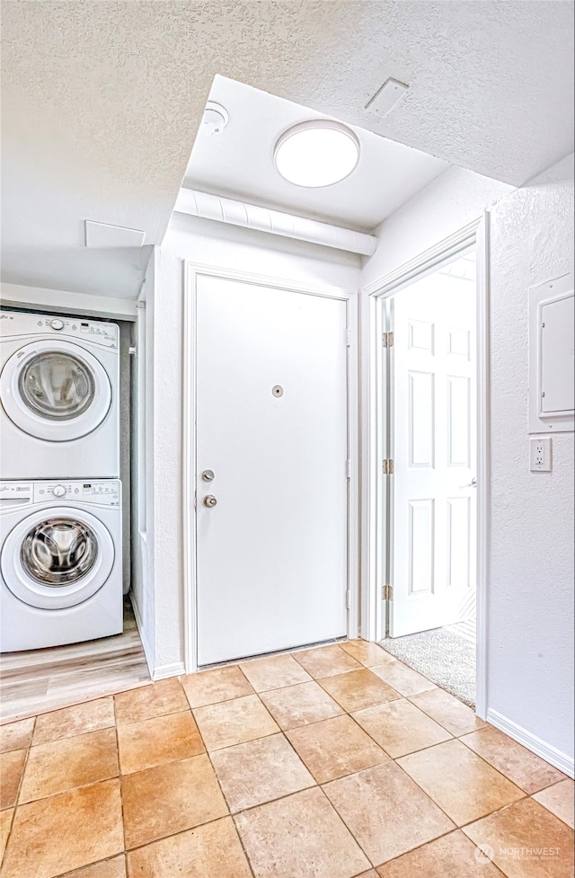 laundry area featuring a textured ceiling, stacked washer and clothes dryer, and light tile patterned floors