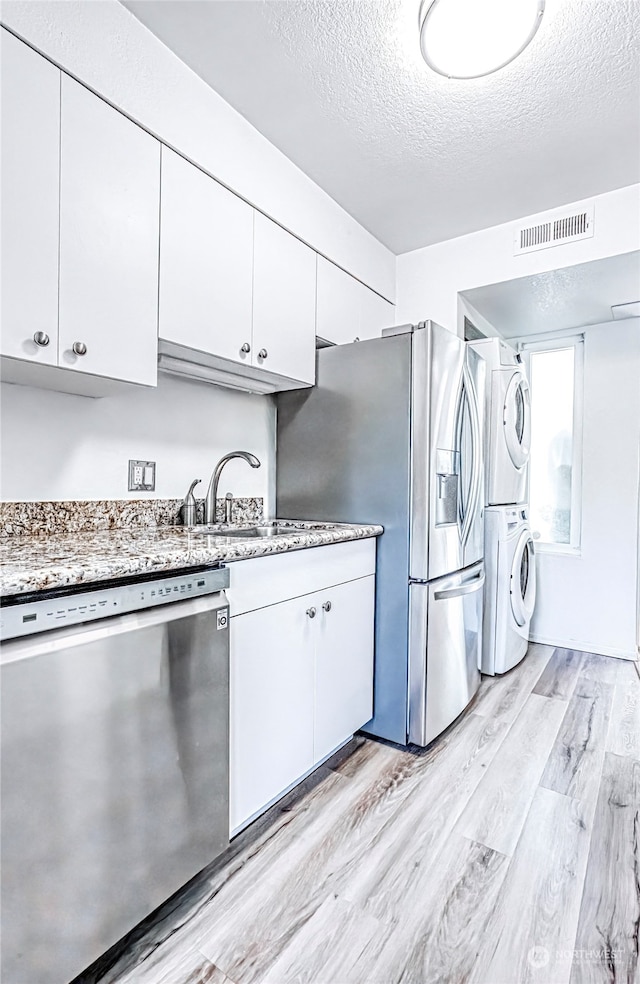 kitchen with stainless steel appliances, white cabinets, light wood-type flooring, and stacked washer and clothes dryer