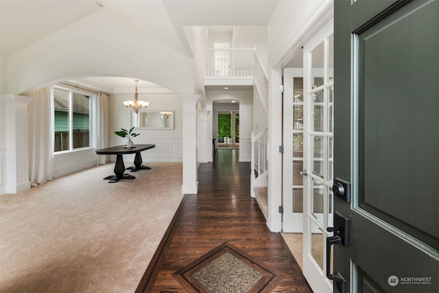 entrance foyer with ornamental molding, a chandelier, dark carpet, and ornate columns