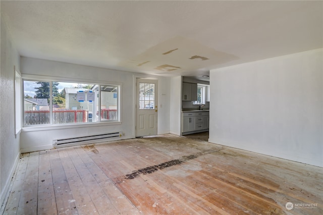 unfurnished living room with a baseboard radiator, plenty of natural light, and hardwood / wood-style flooring