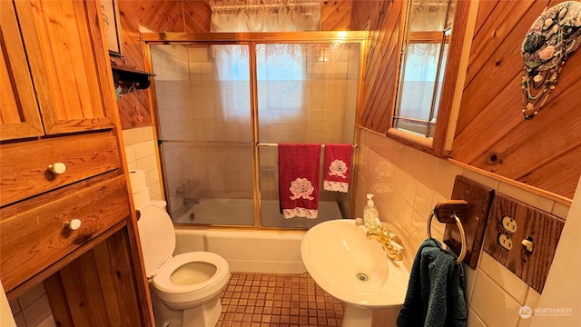 full bathroom featuring combined bath / shower with glass door, tile patterned flooring, wooden walls, toilet, and sink