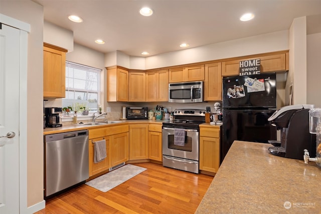 kitchen with appliances with stainless steel finishes, light wood-type flooring, light brown cabinetry, and sink