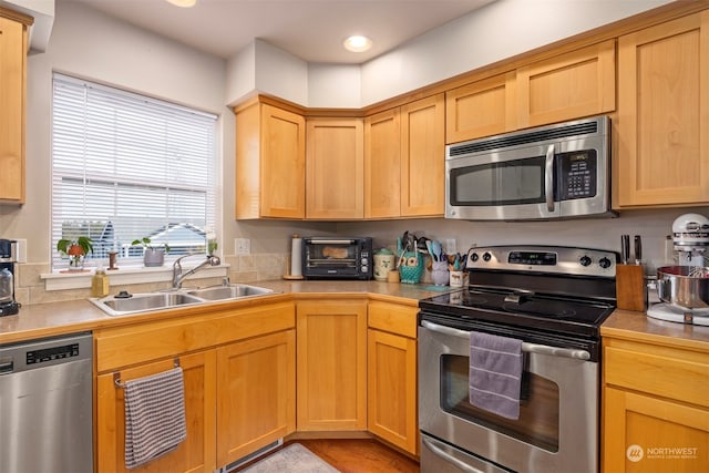 kitchen with appliances with stainless steel finishes, sink, and light hardwood / wood-style floors