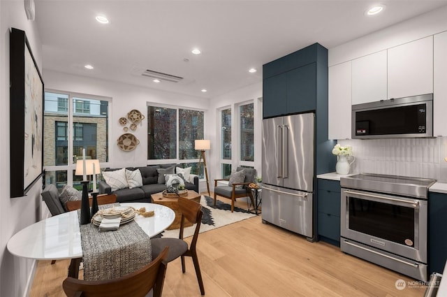 kitchen with tasteful backsplash, blue cabinets, white cabinets, light hardwood / wood-style floors, and stainless steel appliances