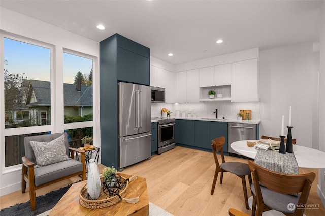 kitchen with blue cabinetry, white cabinetry, stainless steel appliances, tasteful backsplash, and light wood-type flooring