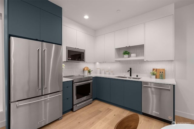 kitchen with blue cabinetry, sink, tasteful backsplash, stainless steel appliances, and white cabinets