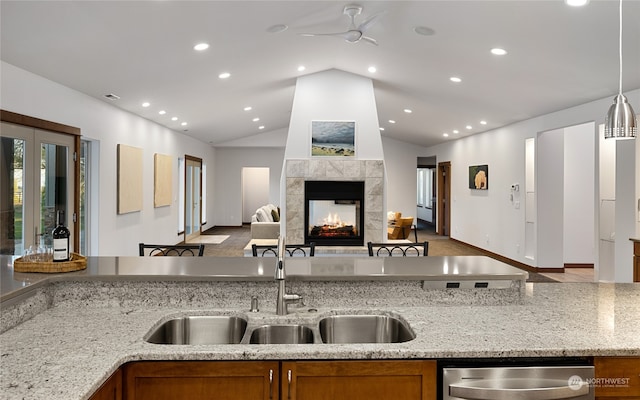 kitchen with light stone counters, pendant lighting, a multi sided fireplace, sink, and vaulted ceiling