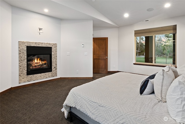 bedroom with vaulted ceiling, a fireplace, and dark colored carpet