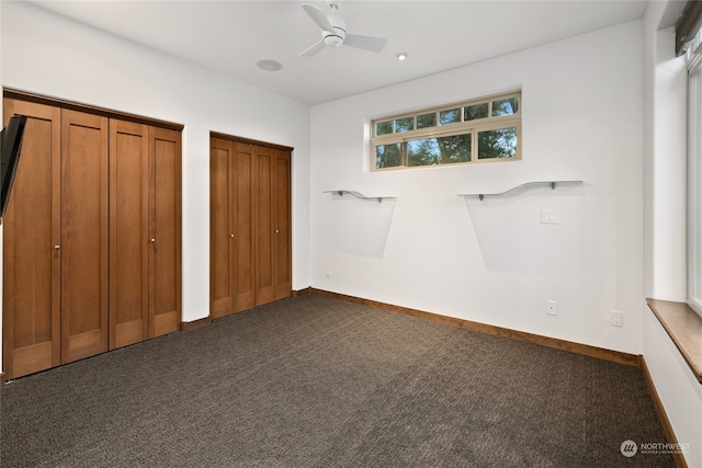 unfurnished bedroom with two closets, ceiling fan, and dark colored carpet