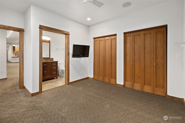 unfurnished bedroom with two closets, ceiling fan, light colored carpet, and ensuite bathroom