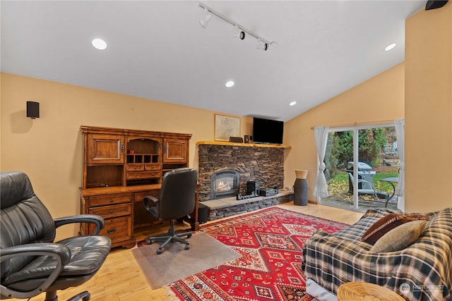 home office with a stone fireplace, light wood-type flooring, rail lighting, and vaulted ceiling