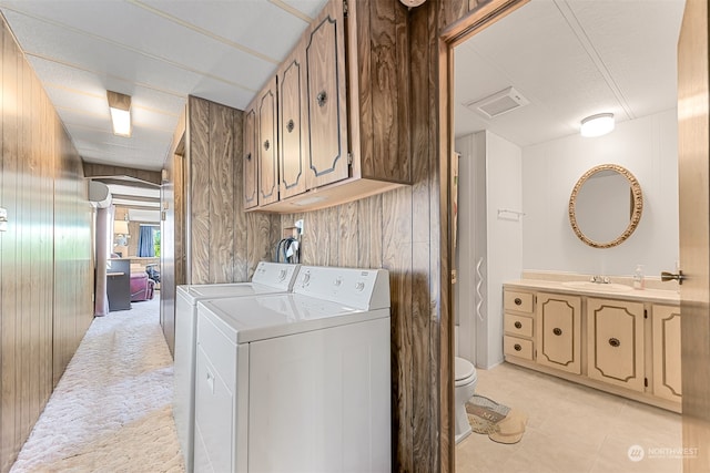 laundry area featuring wood walls, washing machine and clothes dryer, light tile patterned flooring, and sink