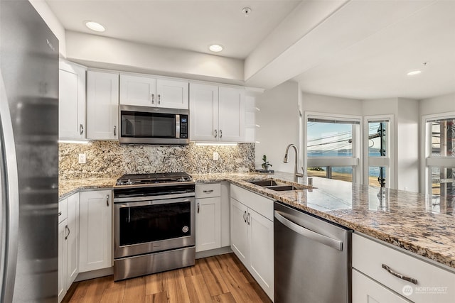 kitchen featuring white cabinetry, appliances with stainless steel finishes, light stone countertops, sink, and light hardwood / wood-style flooring