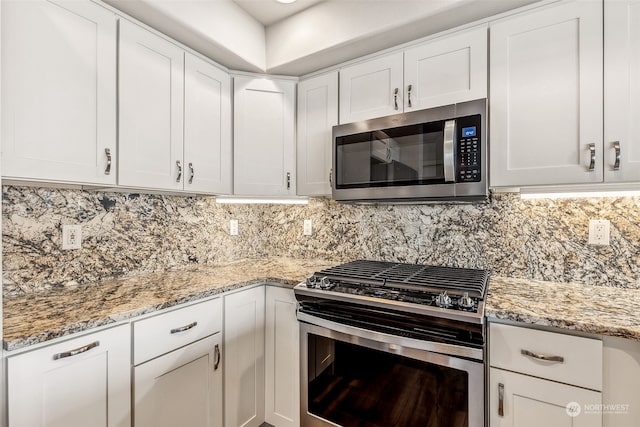 kitchen with stainless steel appliances, white cabinetry, light stone counters, and tasteful backsplash