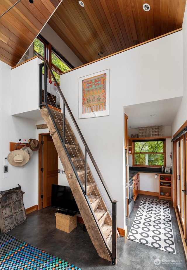 stairway with high vaulted ceiling, wooden ceiling, and finished concrete flooring