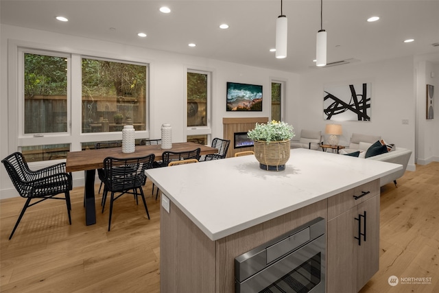 kitchen with light wood-type flooring, decorative light fixtures, a kitchen island, and built in microwave