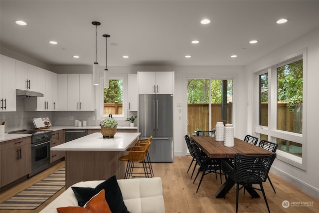 kitchen featuring a center island, backsplash, white cabinets, hanging light fixtures, and stainless steel appliances