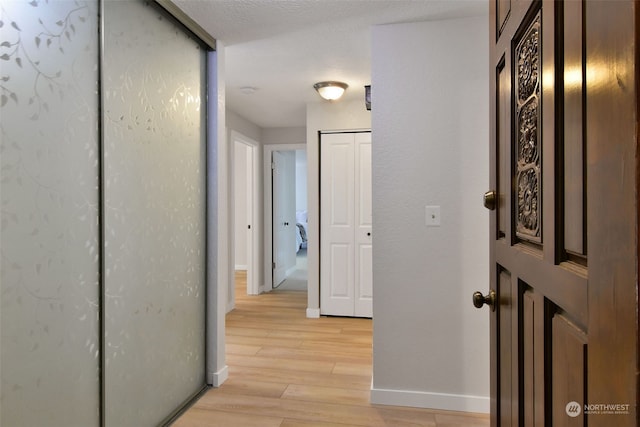 hall featuring light wood-type flooring and a textured ceiling