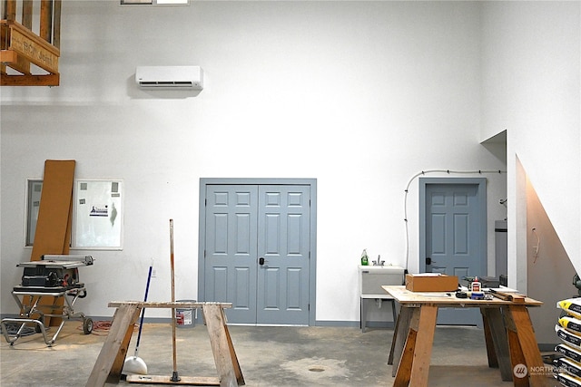 interior space with concrete flooring, a towering ceiling, and an AC wall unit